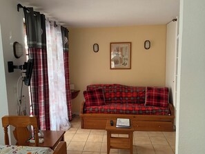 A living room with a sofa, a wooden table, a wall-mounted lamp, and a framed picture. - Apartment T2 Vu mountain 700 meters cable car swimming pool in summer (Cauterets)
