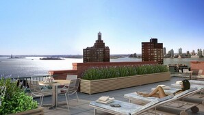 Une terrasse sur le toit offrant une vue sur les toits de la ville et sur l’eau. On y trouve des chaises longues et une table avec des chaises.