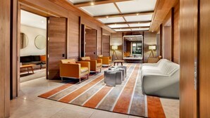 Un hall d’entrée spacieux au design moderne, comprenant un espace de détente central avec des canapés et des fauteuils, un tapis à motifs et un plafond doté d’un éclairage encastré.