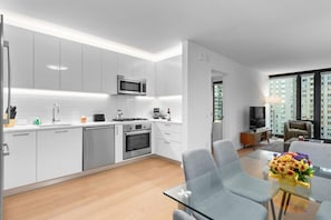 Une cuisine moderne avec des meubles blancs, un four à micro-ondes et un coin repas comprenant une table en verre et des chaises grises.