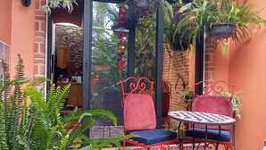 A cozy outdoor seating area with two red metal chairs and a small round table, surrounded by lush green plants and a stone-tiled floor. - Casita Escondida - charming new studio casita for 1 in central Ajijic (Ajijic)