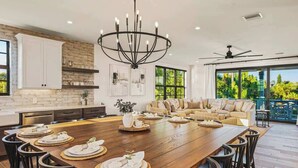 A spacious kitchen with a large wooden table set for dining, a chandelier, and a view of the outdoors. - 2 Homes–2 Pools/Hot Tubs–Steps from Siesta Beach (Sarasota)