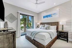 Un dormitorio con una cama grande, un ventilador de techo, una ventana con persianas y vistas a palmeras.