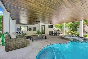 Un área de piscina interior con techo de madera, un sofá de mimbre, una mesa de comedor y una piscina pequeña.