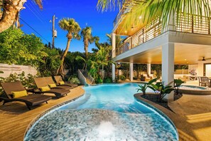 Een zwembad met ligbedden, een jacuzzi en een gebouw met twee verdiepingen en een balkon.