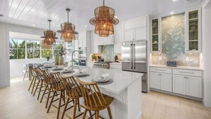 Una cocina moderna con armarios blancos, una isla central con taburetes de bar e iluminación colgante.
