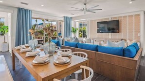 Un comedor moderno con una mesa de madera dispuesta para cuatro personas, asientos tapizados en azul y un televisor montado en la pared.