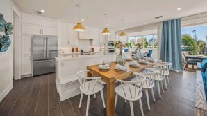 Una cocina moderna con armarios blancos, electrodomésticos de acero inoxidable y una mesa de comedor de madera con sillas blancas.