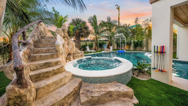 Una piscina con hidromasaje, escalones de piedra y un aro de baloncesto.