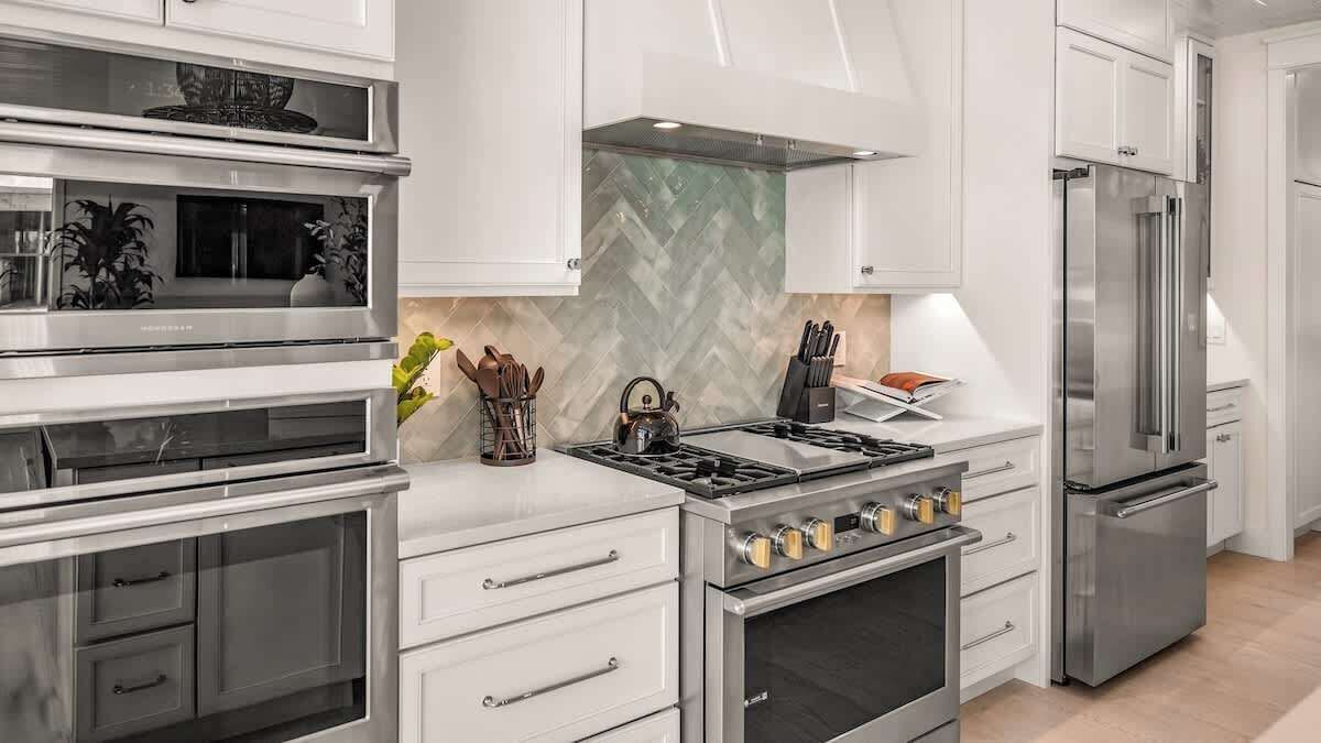 A modern kitchen with stainless steel appliances, white cabinetry, and a herringbone tile backsplash.