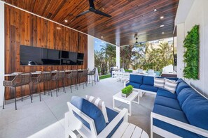 A modern outdoor patio with a wooden ceiling, a bar area with seating, and a sofa set. - New - Dual-home luxury, Rooftop Decks, Sleeps 32 (Siesta Key)