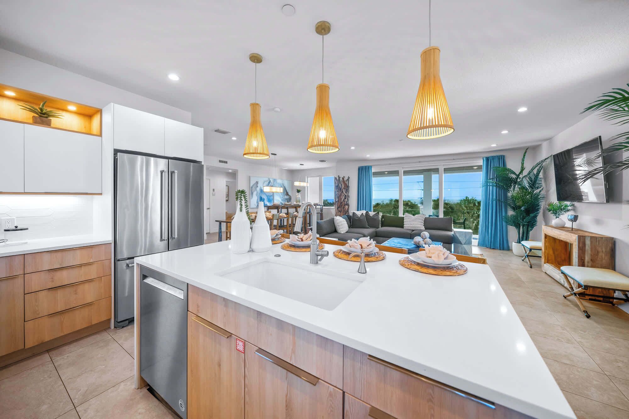 Une cuisine moderne dotée d’un grand îlot central, d’appareils électroménagers en acier inoxydable et de luminaires suspendus.