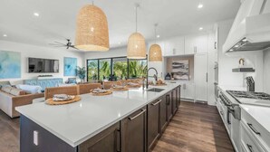 Una cocina moderna con una isla grande, armarios blancos e iluminación colgante.