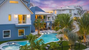 Una casa de dos pisos con piscina, mobiliario exterior y vista al atardecer.