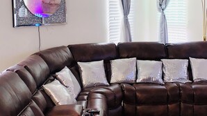 A brown leather sectional sofa with silver cushions, a chandelier, and a decorative mirror with a pink and silver design. - The Presidential Suite (Fort Washington)