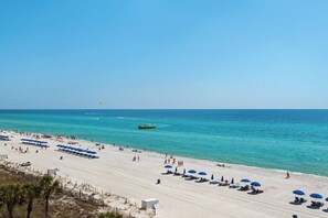 A beach with rows of sun loungers and umbrellas, a boat in the water, and a clear blue sky.