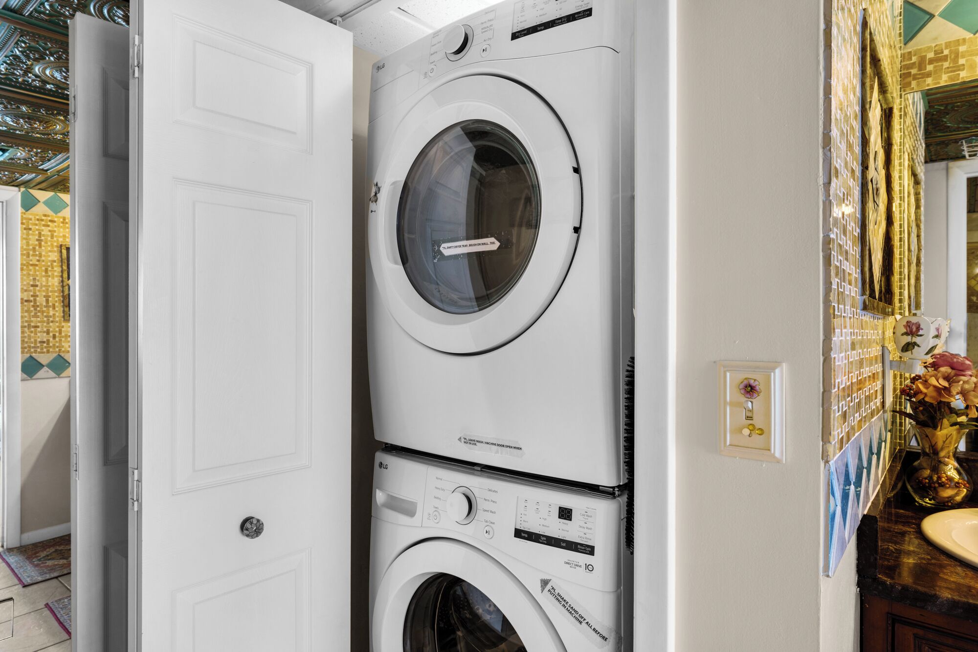 A stacked washer and dryer unit in a room with a tiled floor and a decorative wall.