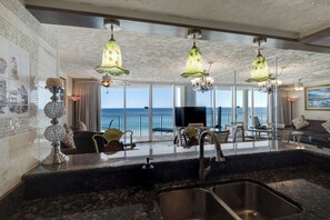 Eine moderne Küche mit einer großen Kochinsel, ein Essbereich mit Meerblick und eine Wohnfläche inklusive Sofa und Dekoration.