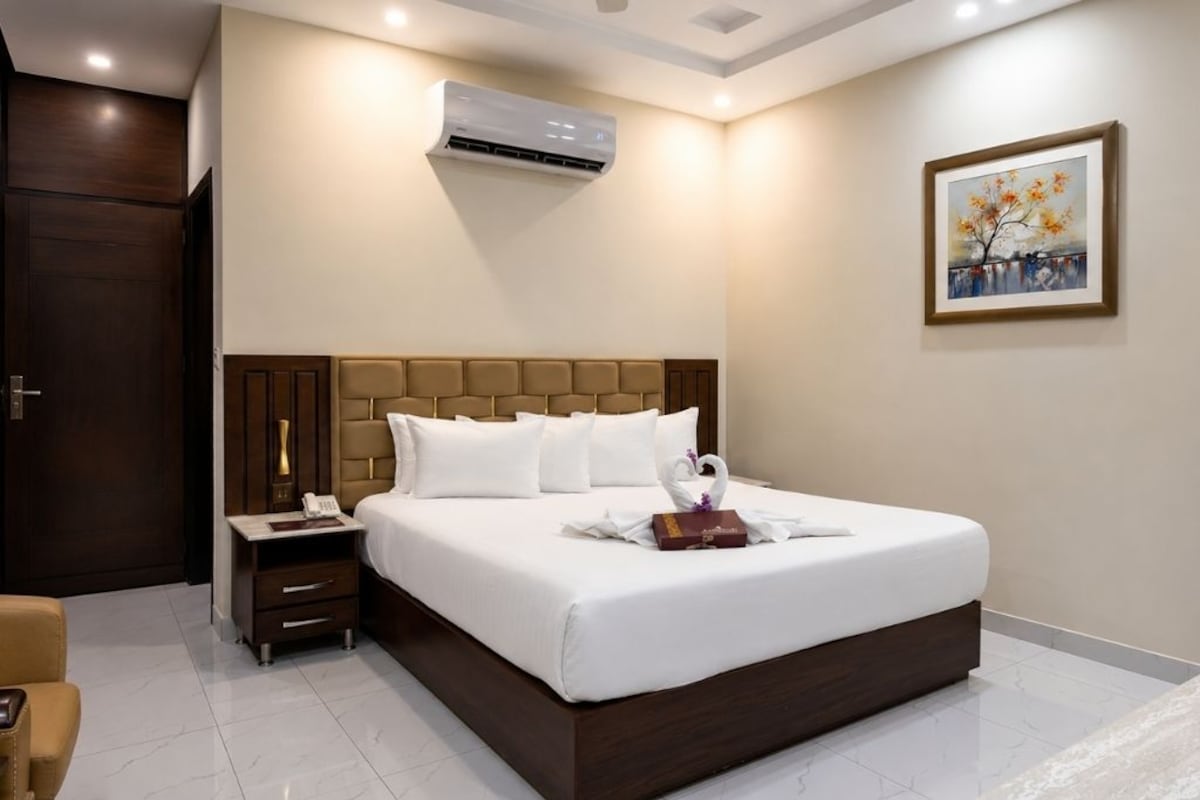 Habitación de hotel con una cama grande, una mesita de noche, una silla y un cuadro en la pared.