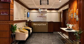 Zona de recepción de un hotel con mostrador, televisor y un cartel que indica la biblioteca.