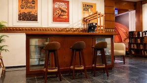 Een bar met drie krukken, een koffieapparaat en ingelijste posters aan de muur.