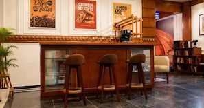 Zona de bar con tres taburetes, una máquina de café y carteles enmarcados en la pared.