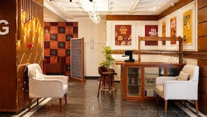 Een hotellobby met een receptiebalie, twee fauteuils, een koffiebar en een muur met posters.