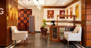 Un vestíbulo de hotel con una recepción, dos sillones, una cafetería y una pared con carteles.