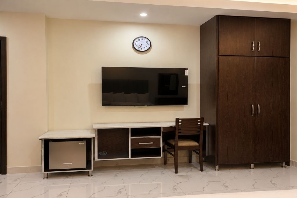 A room with a flat-screen TV mounted on the wall, a wooden cabinet, a small cabinet, and a chair.