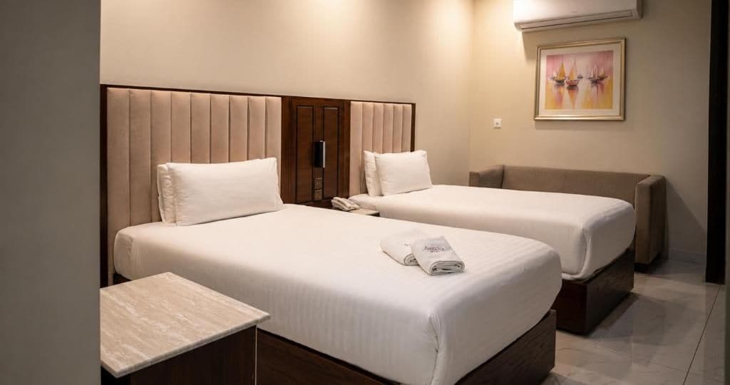 Habitación de hotel con dos camas, una mesita de noche y un cuadro en la pared.