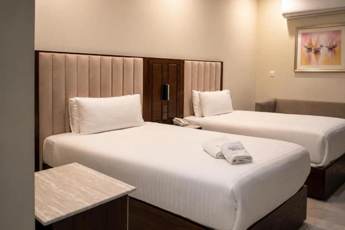 Habitación de hotel con dos camas, una mesita de noche y un cuadro en la pared.