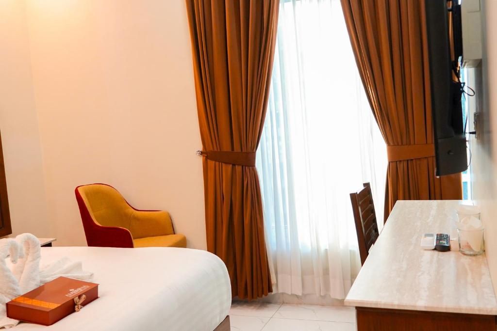 Een hotelkamer met een bed, een gele fauteuil, een eettafel met een afstandsbediening en gordijnen.
