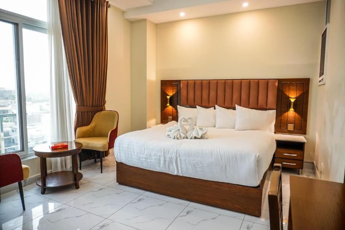 Una habitación de hotel con una cama grande, una silla, una mesita y vistas a la ciudad.