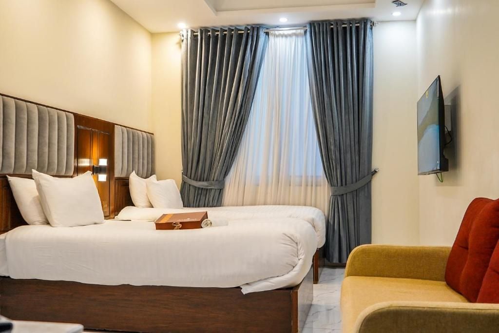 Una habitación de hotel con cama, sofá, televisor y ventana con cortinas.