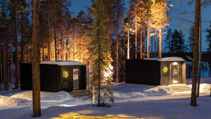 A cabin in a snowy forest at night with a snow circle and a small building with steps leading up to it. - OloResort Levi (Kittilä)