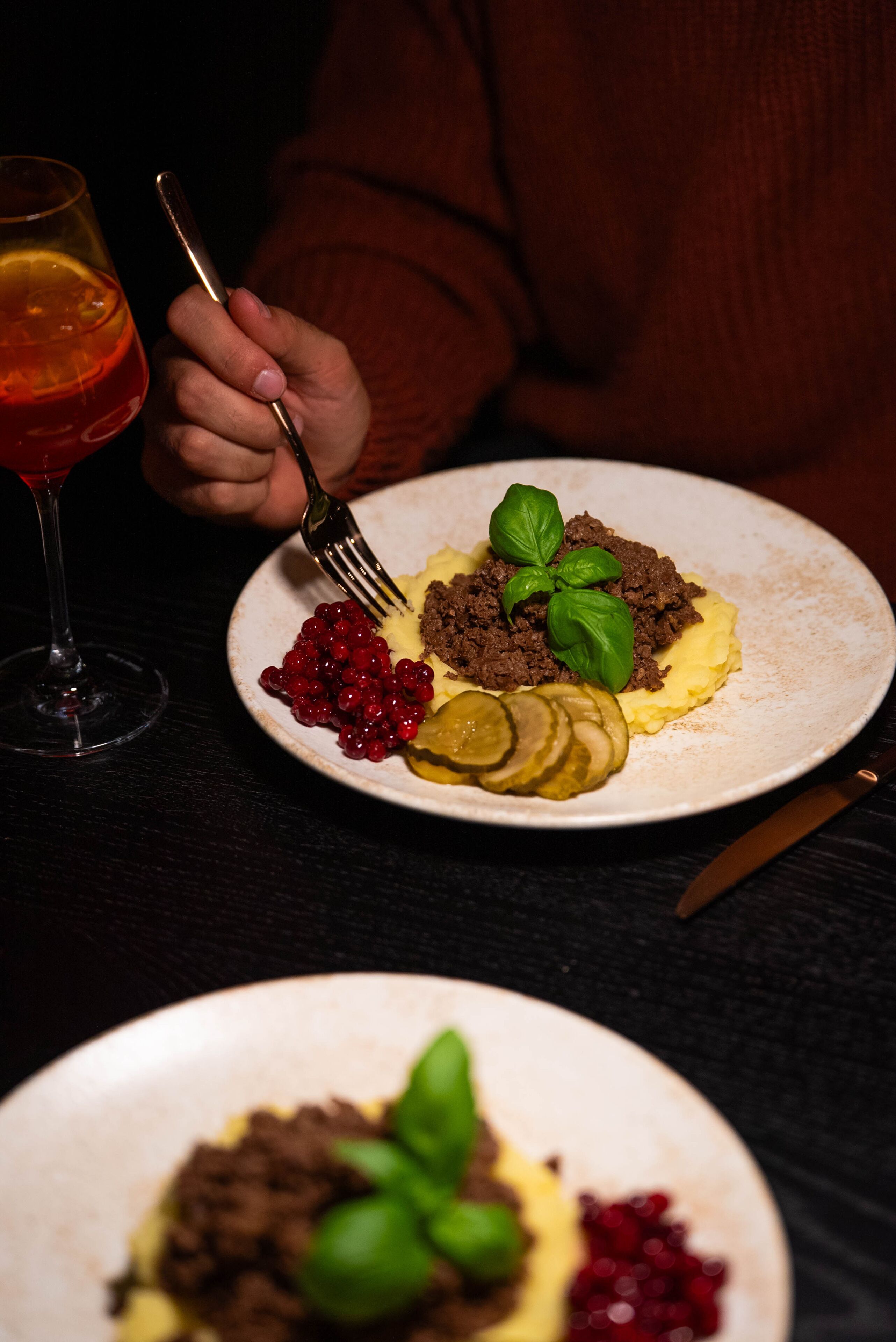 A plate of food with a fork, a glass of red drink, and a knife on a dark table.