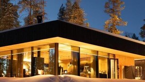 A modern building with large glass windows, surrounded by snow and trees. - OloResort Levi (Kittilä)