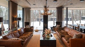 A modern living room with leather sofas, a glass coffee table, and a large window with a view of a snowy landscape. - OloResort Levi (Kittilä)