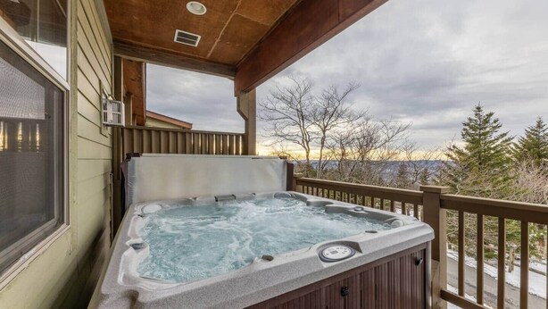 Een hottub op een houten terras met uitzicht op bomen en bergen.