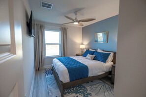 A bedroom with a bed, a ceiling fan, a window with curtains, a bedside lamp, and a framed picture on the wall. - Tranquil Coastal Escape - Just Steps to the Beach - Bikes included (Port St. Joe)