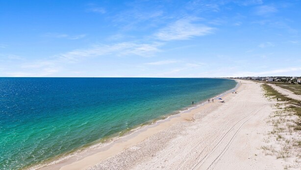 En strand med kristallklart turkost vatten, en sandstrand och några få personer.