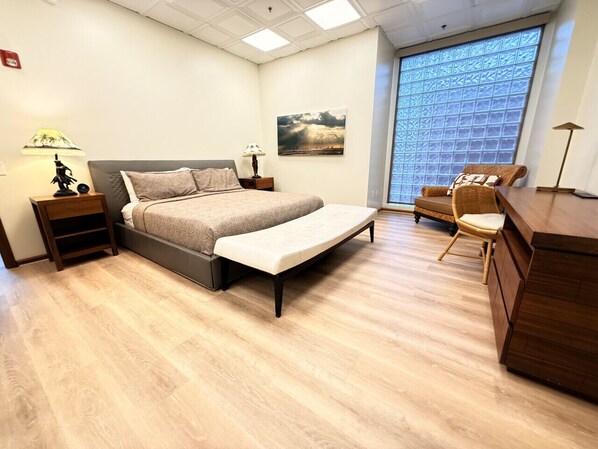 A bedroom with a bed, bedside tables, a chair, a desk, and a window with a view. - Upscale 3BR Luana Waikiki Suite • Sleeps 6 • Walk to Beach (Honolulu)