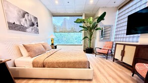Un dormitorio moderno con cama, un ventanal grande, una planta y un televisor.