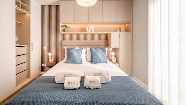 A modern bedroom with a bed, bedside tables, a wardrobe, and a hanging light fixture. - GuestReady - Maleo Living Apartments - 10C1 (Lisbon)