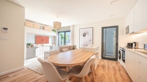 Moderni keittiö, jossa on ruokailutila. Keittiössä on puinen pöytä ja tuolit, sisäänrakennettu uuni sekä suuri ikkuna, jossa on sälekaihtimet.