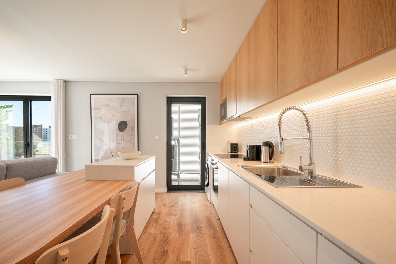 Een moderne keuken met houten kastjes, een roestvrijstalen spoelbak en een eethoek met een houten tafel en stoelen.