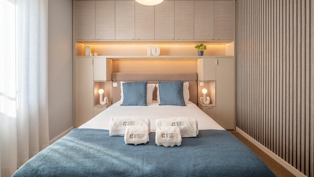 Et moderne hotelværelse med seng, sengeborde, lamper og en hylde med pynt.