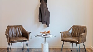 Deux fauteuils en cuir, une petite table ronde avec un livre ouvert et un croissant, et un manteau accroché au mur.