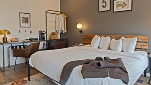 Een hotelkamer met een groot bed, een bureau met stoel, een kapstok en een wandlamp.