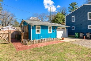 Una casa pequeña de un piso con fachada azul, un garaje y un patio trasero cercado.